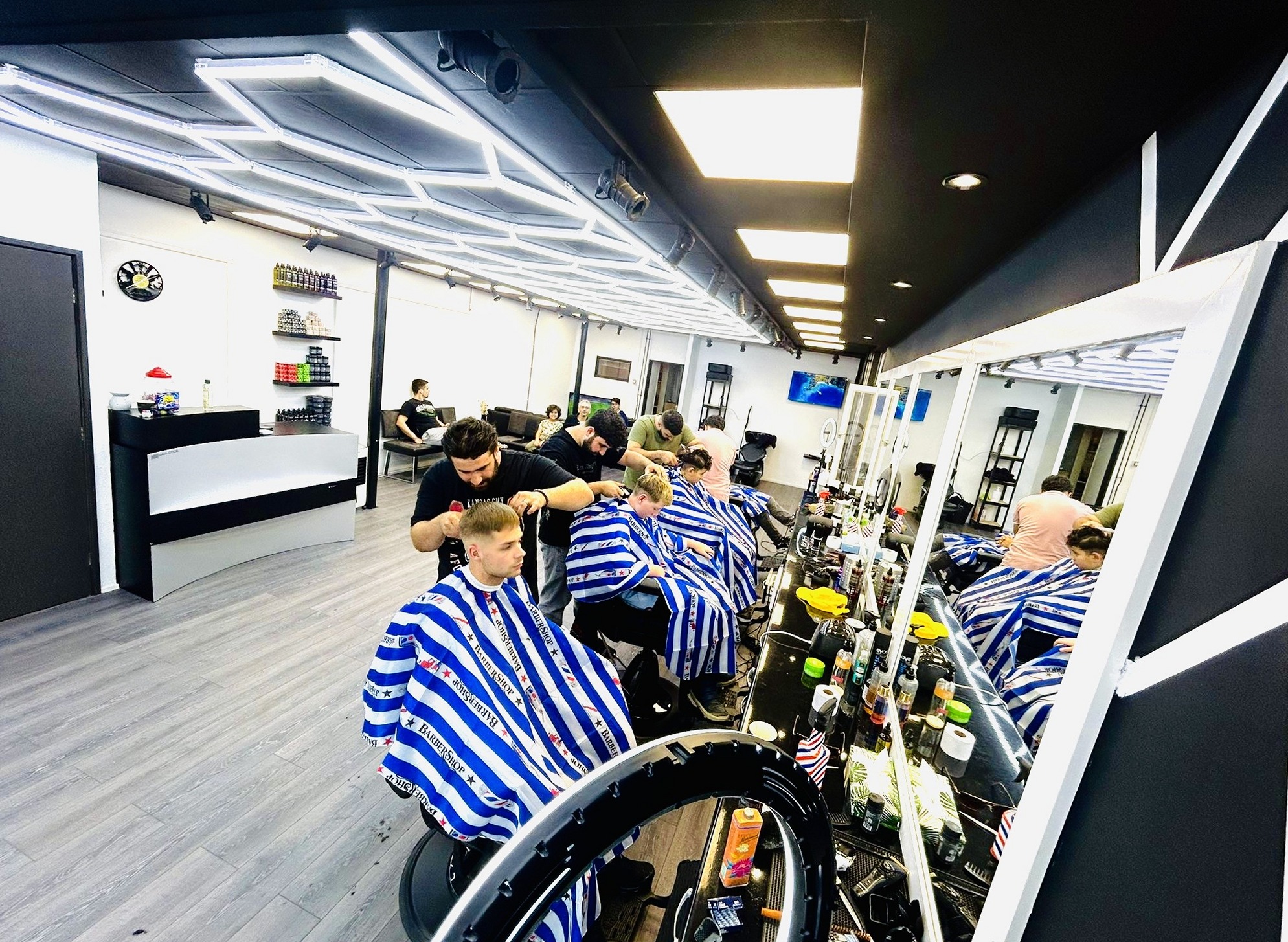 Een rij kappersstoelen met klanten in gestreepte capes voor de spiegelwand