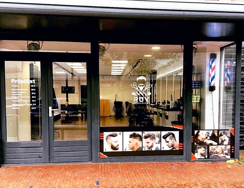De winkelpui van Roy Barbershop met het ROY-logo op het raam en een kapperspaal
