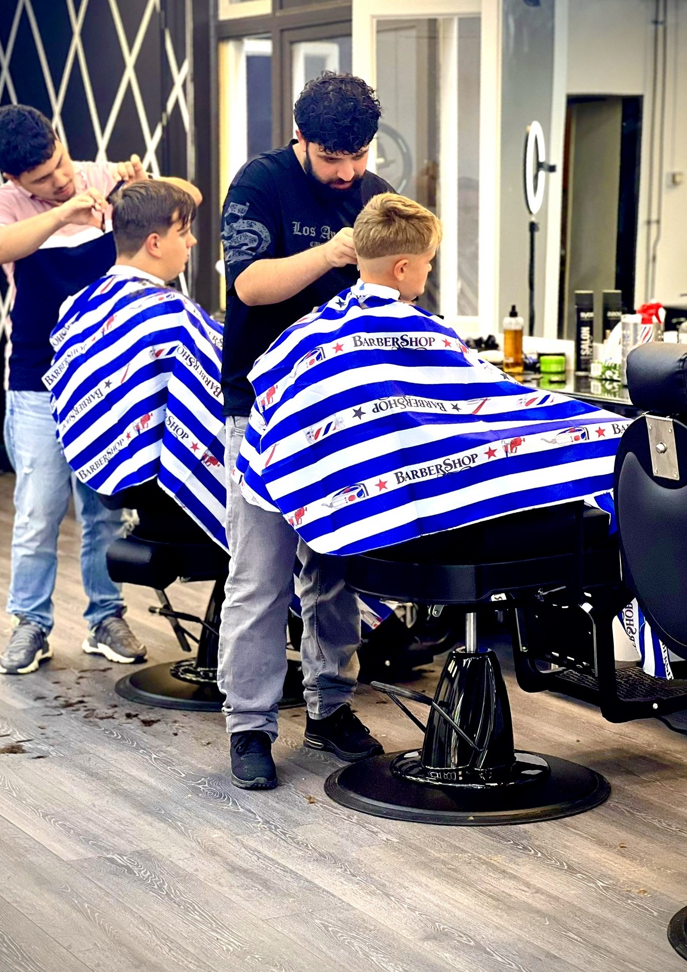 Twee kappers van Roy Barbershop knippen twee klanten in blauw-wit gestreepte capes